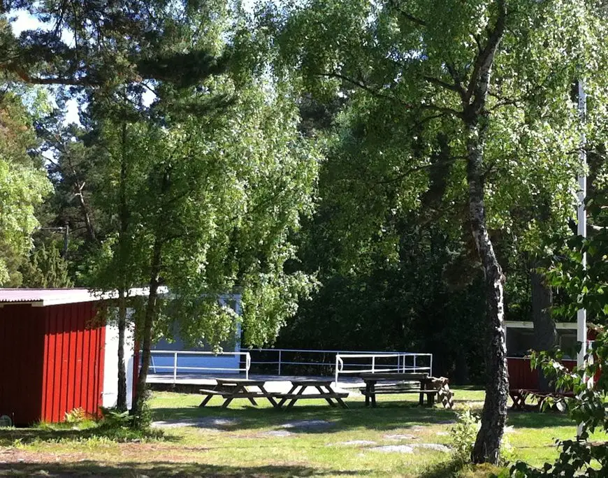 Bänkar och bord under träd vid ställplatsen på Aspö